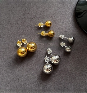 Detail of high-polished gold and silver ball stud earrings in various sizes on grey texture