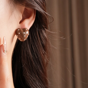 Macro view of a brown heart-shaped earring with white polka dots worn on ear