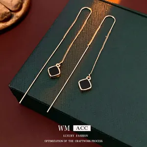 Elegante goldene Durchziehohrringe mit schwarzen quadratischen Anhängern auf einer Box