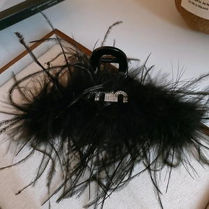 Gros plan sur une pince à cheveux luxueuse en plumes noires avec logo M serti de strass
