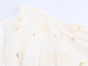 Détail du col en V avec broderie florale délicate et boutons en perles sur robe blanc cassé
