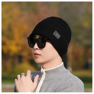 Detail of black ribbed knit beanie with white logo patch shown on a model outdoors