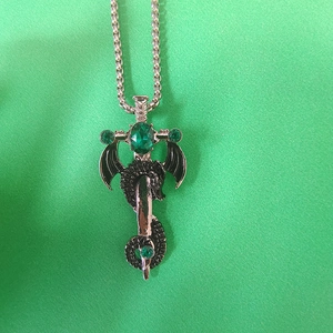 Gros plan d'un pendentif épée vintage avec des ailes de dragon noires et gemme verte