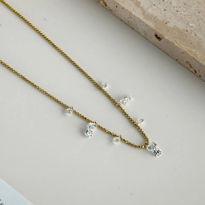 Detailed view of elegant gold beaded necklace featuring dangling clear cubic zirconia stones