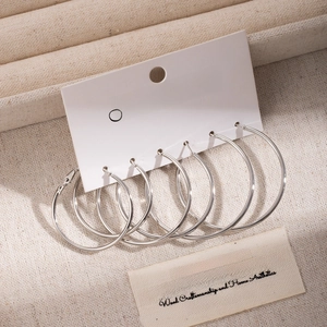 Three pairs of silver hoop earrings in different sizes displayed on a natural linen card