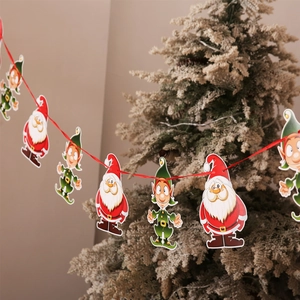 Close-up of Santa and elf paper banners hung with red ribbon against a Christmas tree