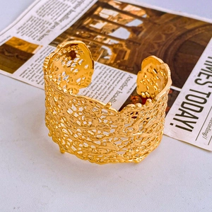 Macro shot of wide gold hollow cuff bracelet with glossy lava texture on vintage paper