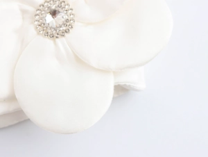 Close-up of white satin 3D flower detail with sparkling rhinestone center on crop top
