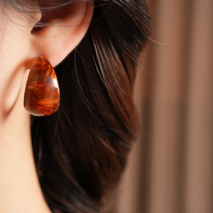 Side view detail of a tortoiseshell resin amber hoop earring worn by a model