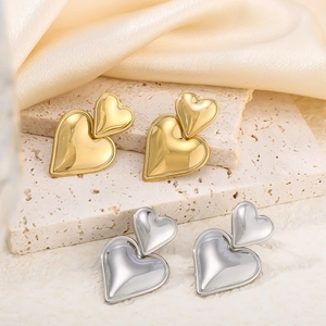 Detail view of gold and silver double heart drop earrings on a soft silk background