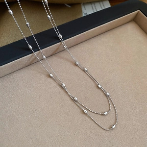 Detail shot of silver metallic rice bead necklace on a beige velvet display tray