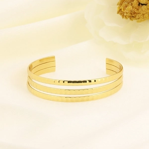 Macro detail of gold layered cuff bracelet featuring hammered texture on satin backdrop