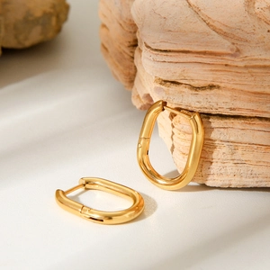 Detailed view of polished gold oval hoop earrings resting on a natural stone surface