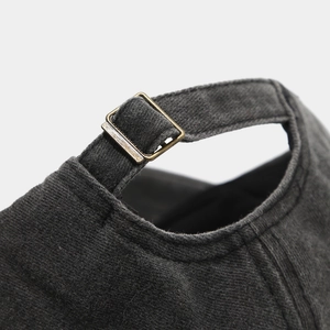 Detailed macro view of the antique brass metal buckle on a washed dark gray baseball cap