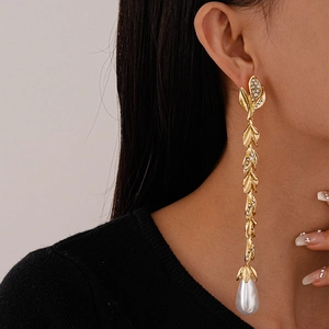 Close-up of gold leaf-shaped tassel earrings with pavé diamonds and a teardrop pearl drop