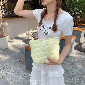 Pale yellow quilted heart pattern clutch bag held by model in outdoor setting