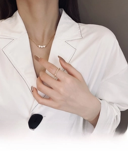 Close-up of minimalist gold necklace with three pearls and beaded ring on model