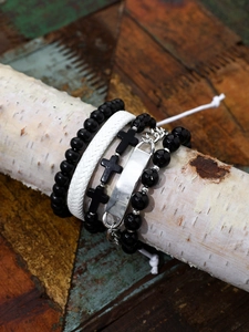 Detail of layered hip-hop bracelets with cross beads and leather on a wood stand