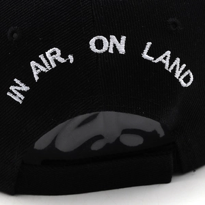 Detail of black baseball cap rear with white IN AIR, ON LAND embroidery and velcro strap