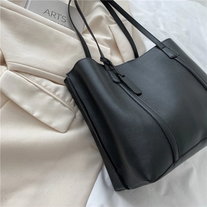 Minimalist black leather tote bag for women shown on white linen with a beige blazer