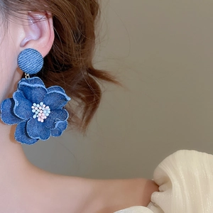 Detailed view of blue denim fabric flower earrings with pearl accents on model