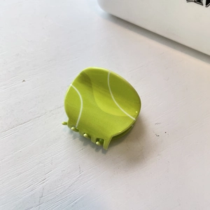 Close-up of a vibrant neon green tennis ball hair claw clip on a white wooden surface