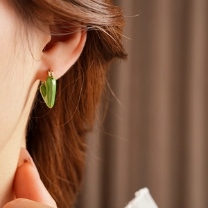 Close-up of vintage green enamel heart earrings with gold trim on a female model