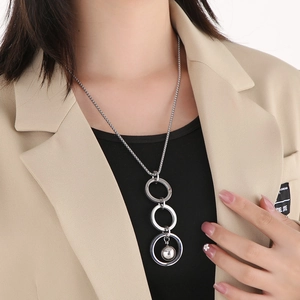 Close-up of three interlocking silver rings and metal ball pendant on long chain