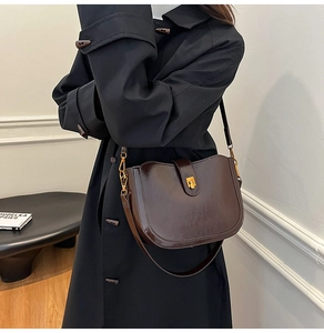 Close-up of matte dark brown saddle bag with gold metal buckle on black coat