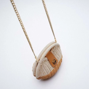 Detail of half-round woven straw bag with brown leather flap and golden chain strap