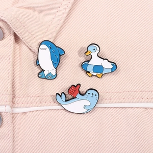 Detailed close-up of cartoon enamel pins featuring a blue shark, duck, and seal on pink denim