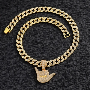 Macro detail of iced-out Shaka sign pendant on a golden Cuban link chain for men