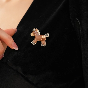 Detail of a gold horse brooch with brown enamel and snowflake charm on black velvet