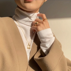 Polished gold U-shaped pendant necklace and minimalist stackable rings worn by a model