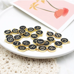 Close-up of round black enamel letter charms with gold finish in a ceramic dish