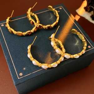 Dettaglio di orecchini vintage a forma di C placcati in oro con occhio di tigre e perla