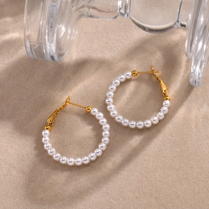 Detailed view of C-shaped gold hoop earrings with white pearls on a sandy texture background