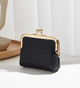 Mini black woven coin purse with gold metal clasp on a wooden tray with stone decor