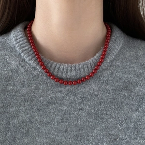 Gros plan d'un collier de perles en verre rouge vintage sur un pull gris de style français