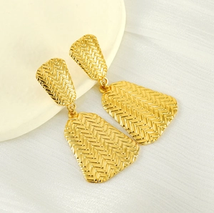 Detail of gold geometric earrings with elegant woven texture on white fabric background