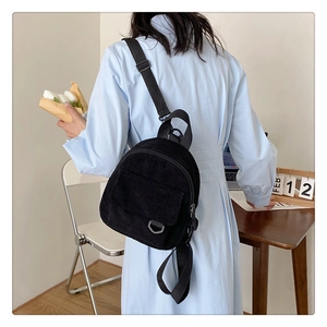 Rear view of a black corduroy mini backpack on a model in a minimalist home setting