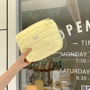 Detail of light yellow quilted makeup bag with heart pattern held by hand