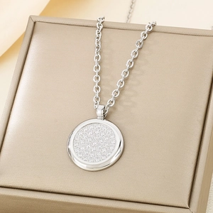 Close-up of a silver circular pendant necklace with sparkling pavé rhinestones in a gold box