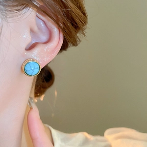 Detail of round vintage turquoise stud earring with gold frame worn by a model