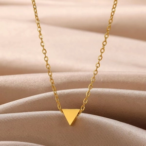Macro detail of a minimalist gold triangle pendant on a fine chain with satin fabric