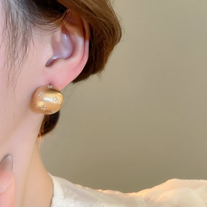 Detailed close-up of matte gold spherical stud earring featuring a tiny star-set zircon