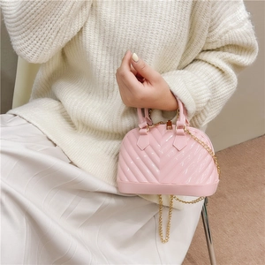 Pink jelly handbag with V-quilt texture and gold chain strap held by a model