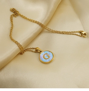 Macro de pendentif en or 18K avec lettre G et nacre posé sur un tissu en soie dorée