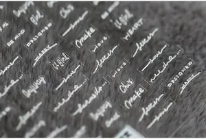 Detail of 5D white embossed nail stickers with cursive English text on a plush background