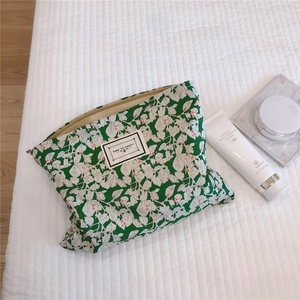 Close-up of green leaf floral makeup bag with Time to Party label on white bedding